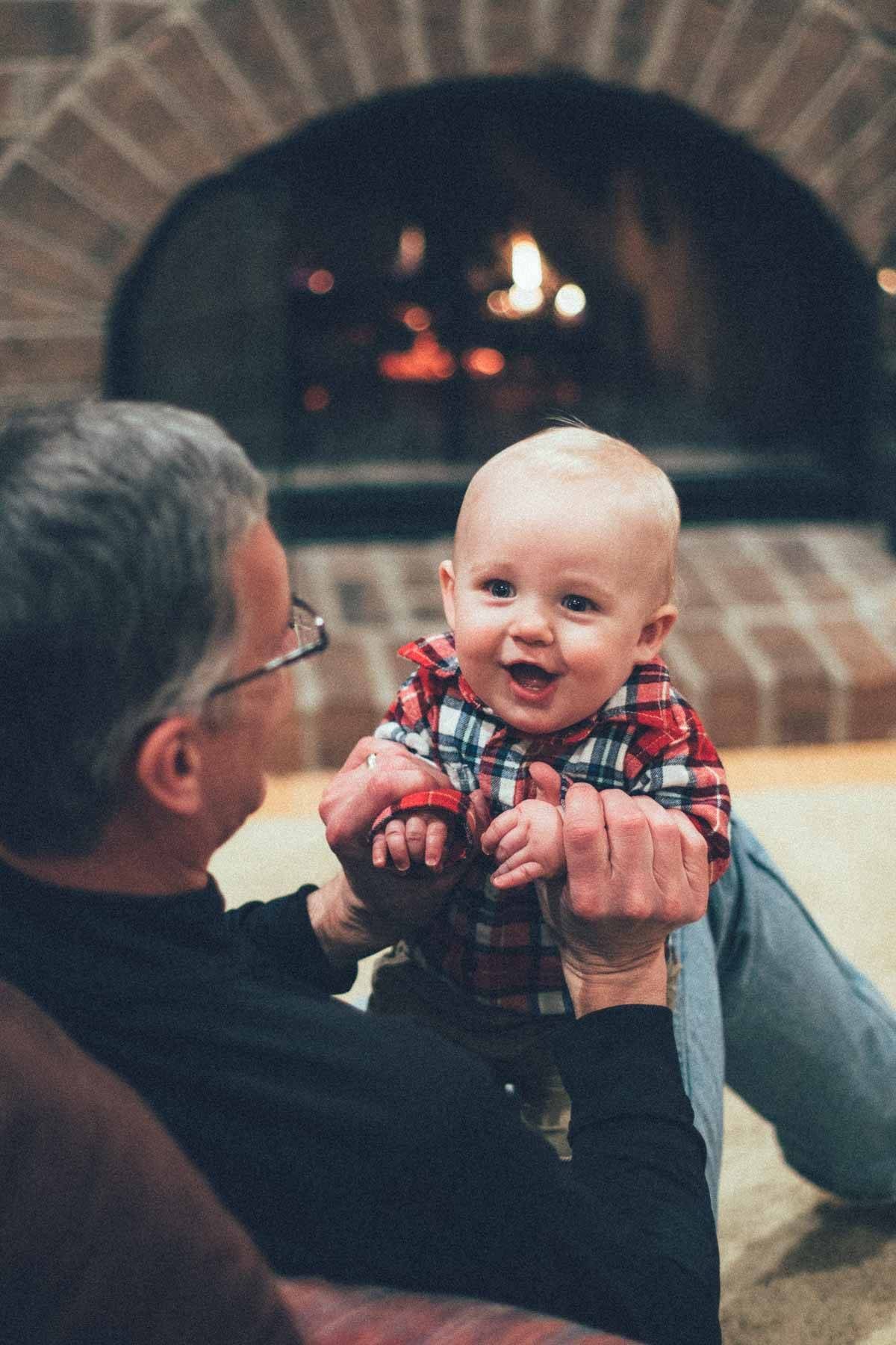 Baby smiling near a fireplace.