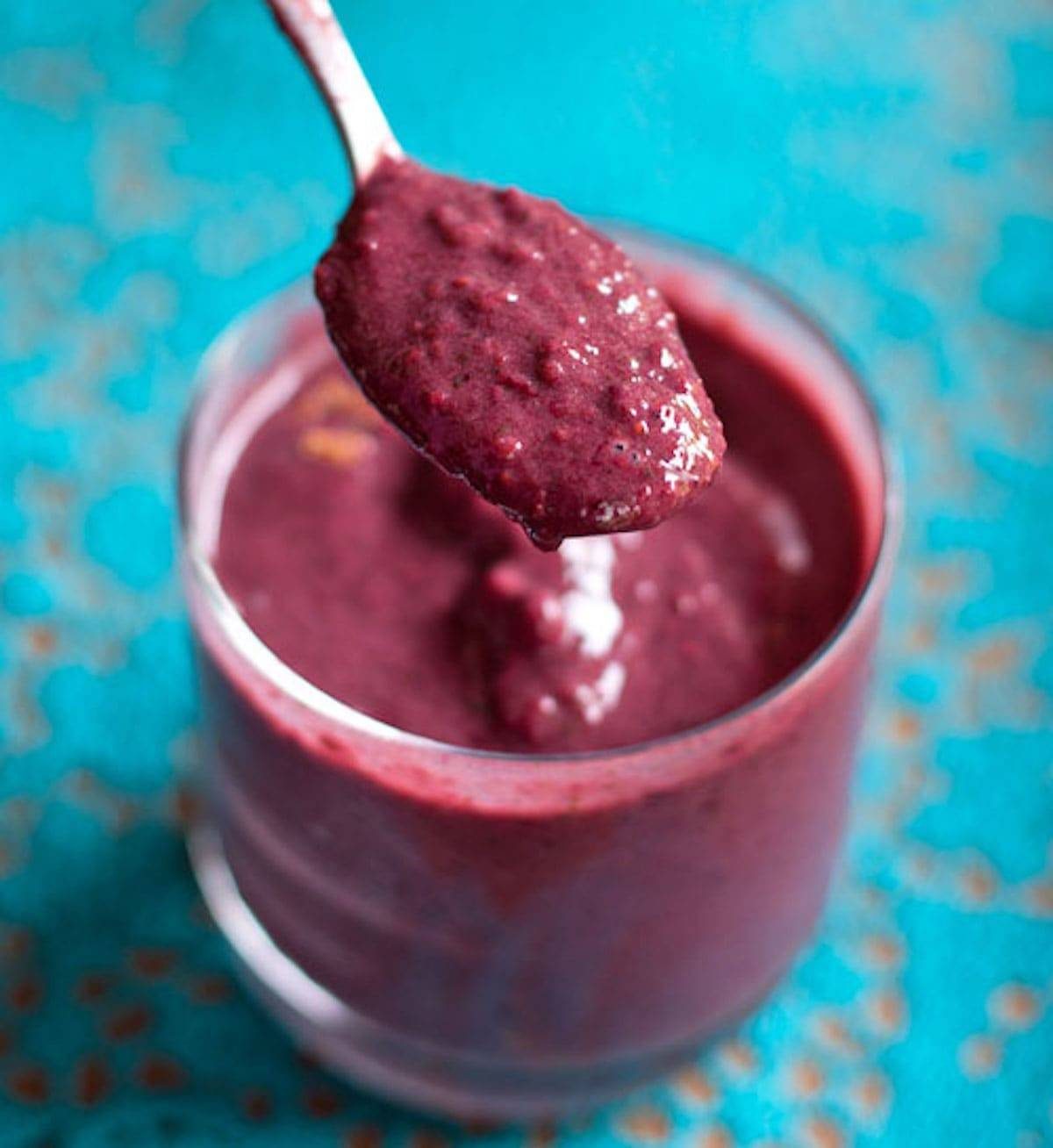 Berry green smoothie in a glass and on a spoon.
