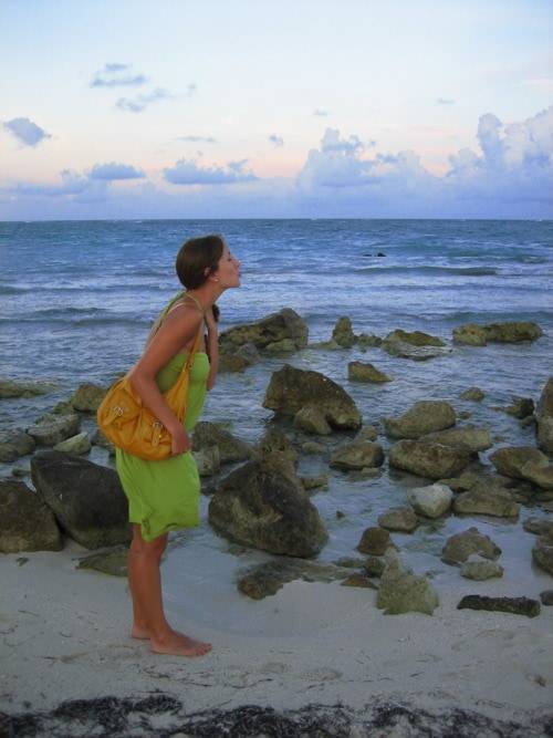 Woman wearing a green dress standing in the sand near the ocean water.