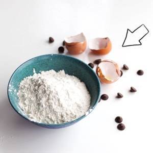 Eggs, flour, and chocolate chips near a blue bowl.
