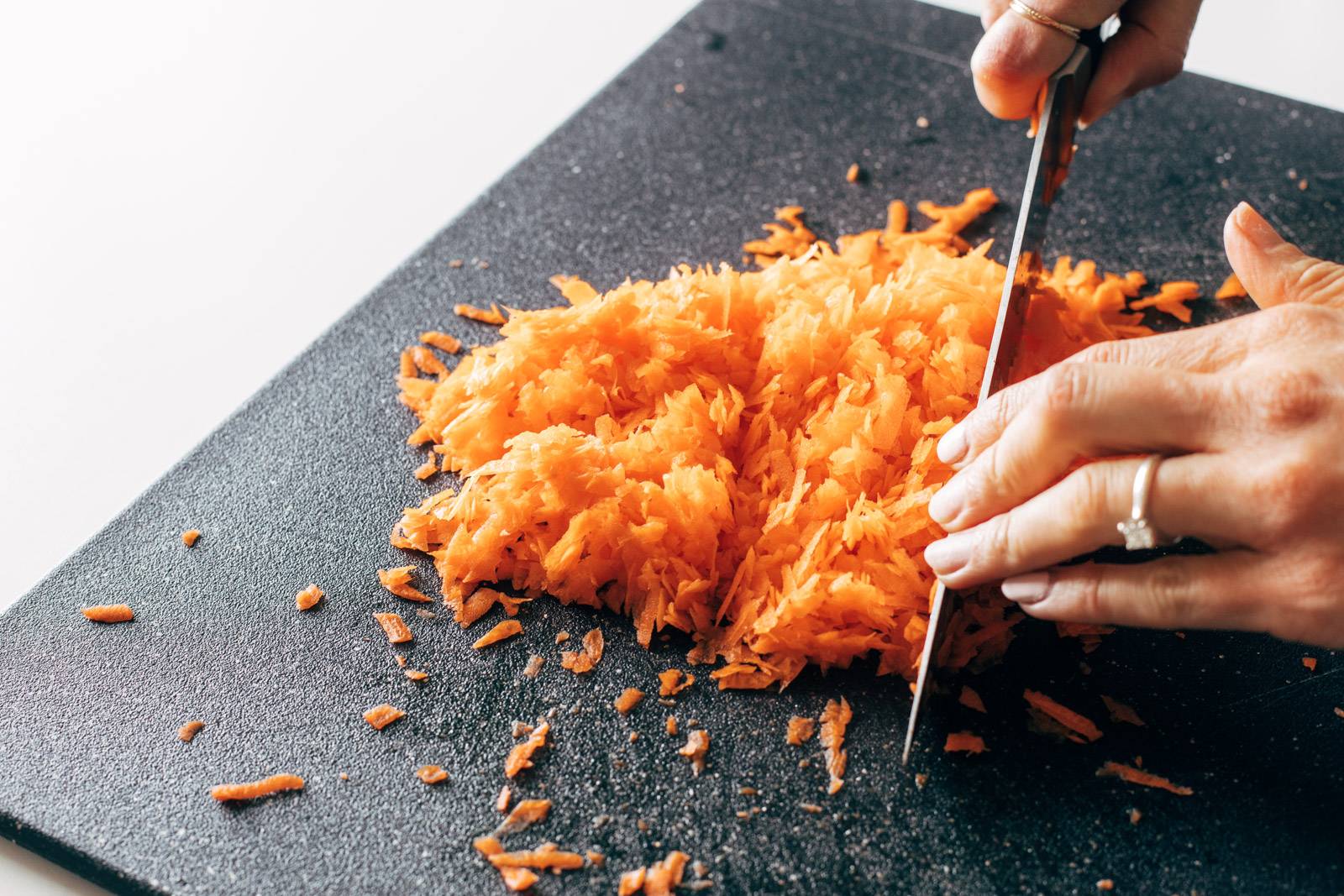 Chopping grated carrots on a cutting board.