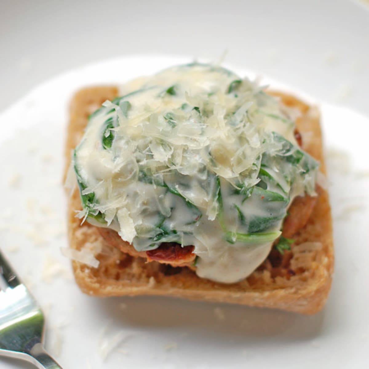 Garlic Parmesan Burger with Creamed Spinach Sauce on a white plate with a fork.