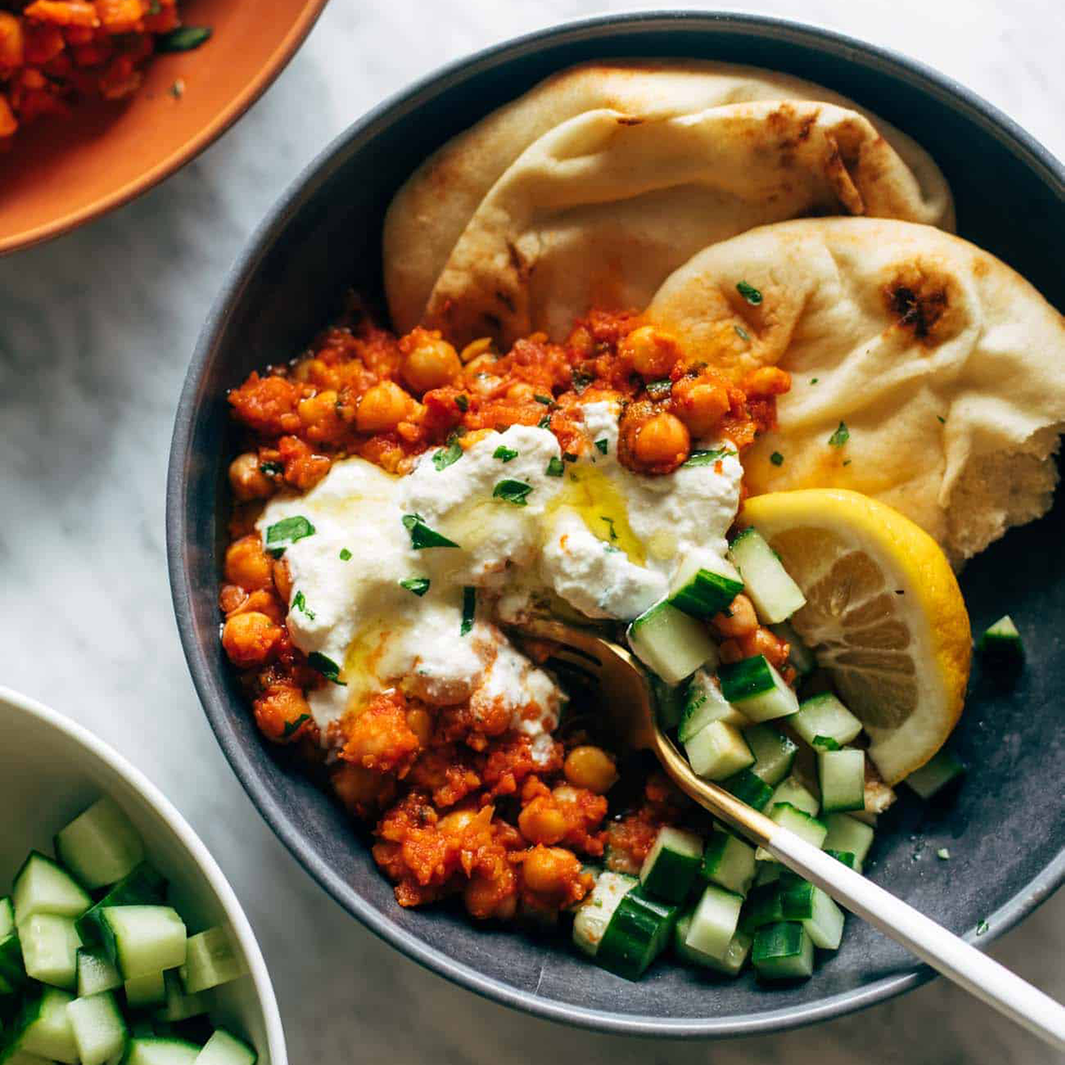 Harissa chickpeas in a bowl with cucumber, naan, and whipped feta.