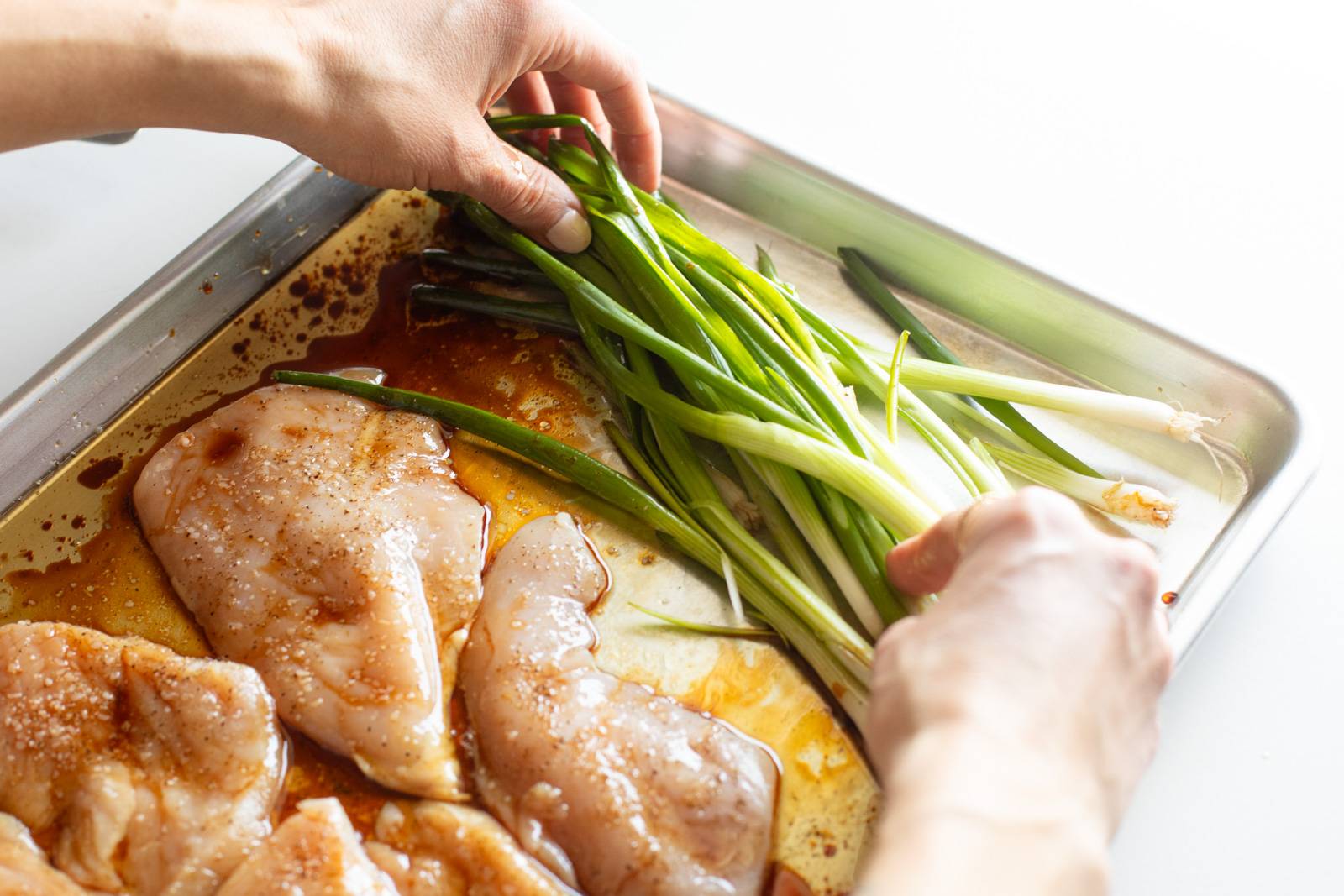Tossing scallions in oil on a sheet pan.